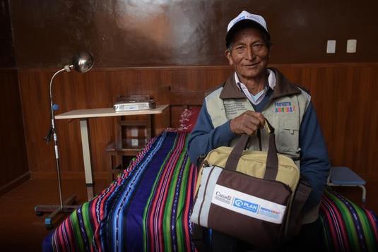 An Arriba-trained midwife carrying a Plan-branded supply bag and smiling at the camera