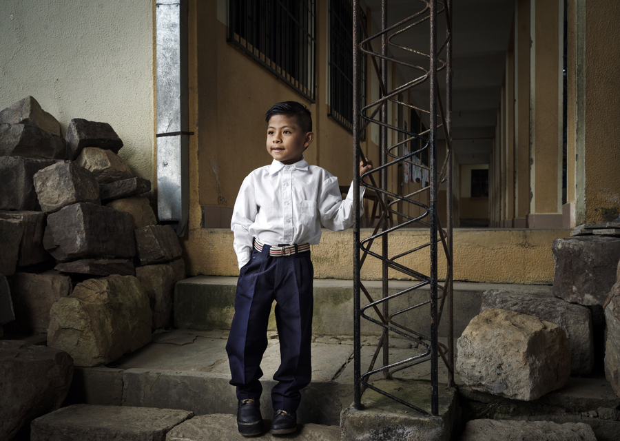 A young boy with mobility challenges stands on uneven steps at his school, showing the lack of accessible facilities for children with disabilities in Bolivia.