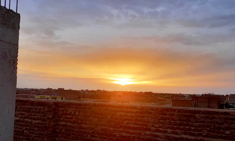 A vibrant sunrise seen from a rooftop, with orange and purple hues lighting up the sky above a city in Sudan.