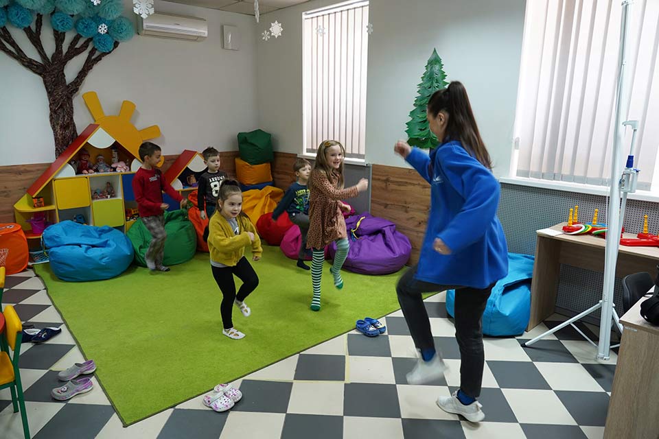 A woman in a classroom leading a group of children in a fun activity.