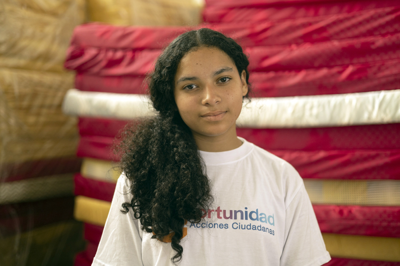 A teenager in a white t-shirt looks straight to camera.
