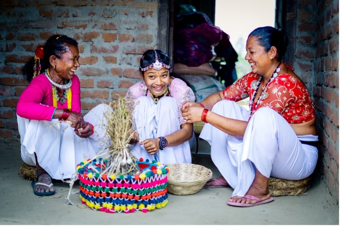 Two women and one girl laughing with each other while sitting down and weaving baskets