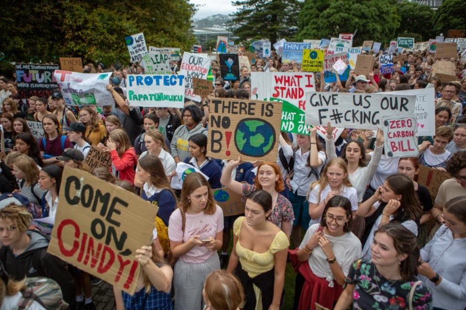 A large group of girls and youth stand together at a protest, some holding signs demanding climate action. 