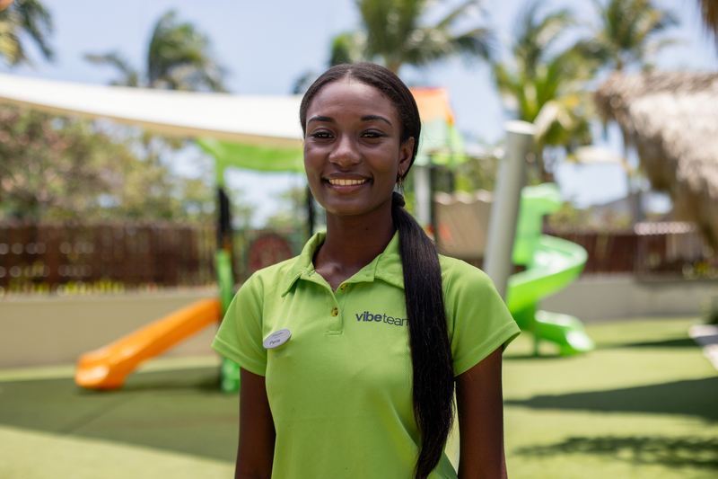 A young woman wearing a highlighter-green T-shirt standing outside in a play area for kids.