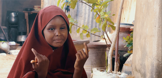 A young girl wearing a maroon hijab while holding up her hands and smiling.