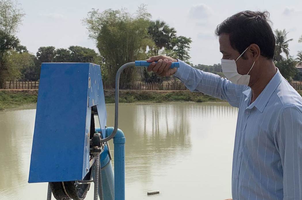 A community leader operating a pump outside the newly created pond