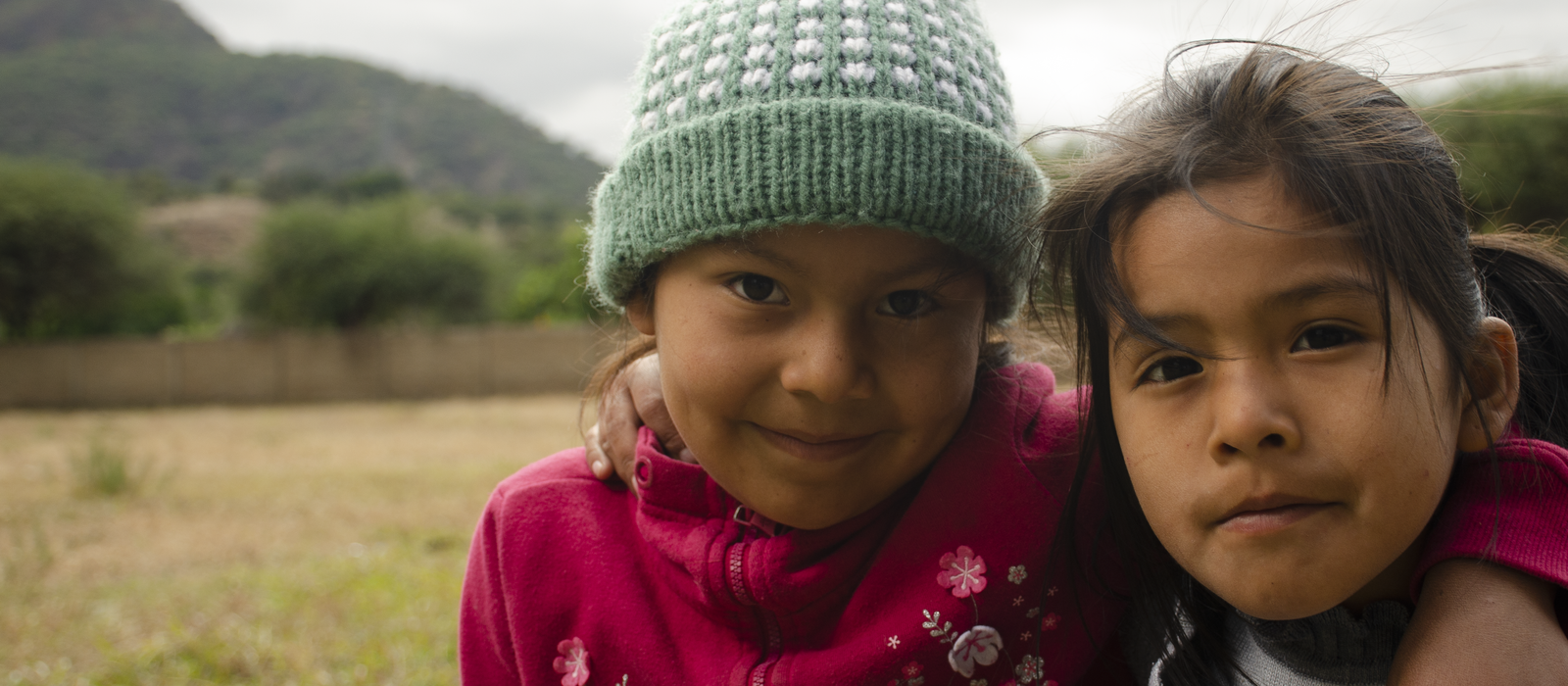Two girls, in a field, one with an arm over the other's shoulder 