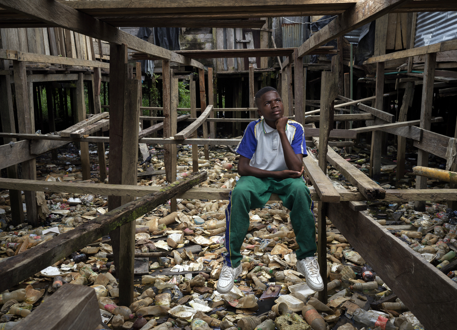 A teenage boy sits in a garbage-filled lot in Chocó, Colombia, determined to pursue education despite poverty and flooding.