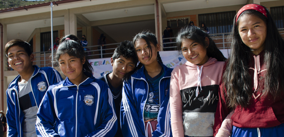 Four school-aged girls and two school-aged boys stand together shoulder to shoulder.