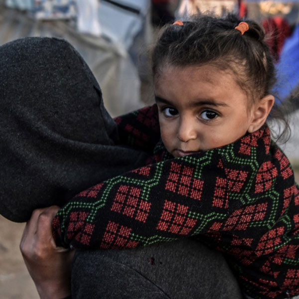 A photo of a young child looking directly into camera as theyre being carried on the shoulders of another youth in Rafah. 