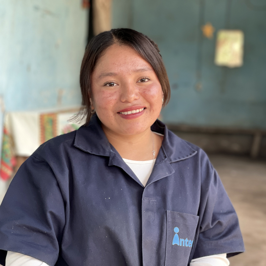 A young woman smiling in a blue jumpsuit, representing women's skills training and economic empowerment.