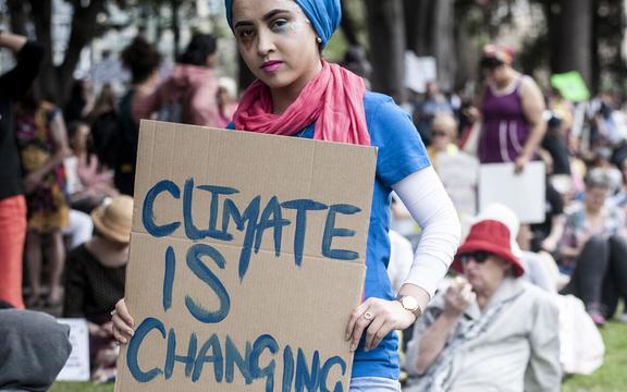 A young girl holding a sign that reads, climate is changing, why aren’t we?