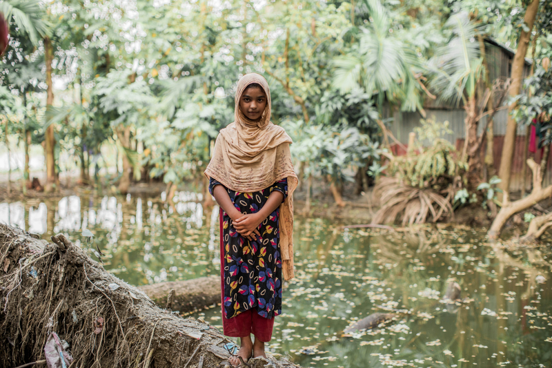 A girl standing on a fallen tree surrounded by flood waters.
